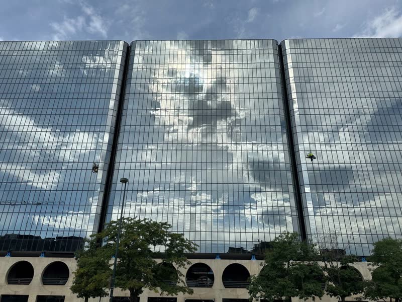 Two S&K rope technicians on a mirrored glass tower in Denver, clouds reflected in the glass