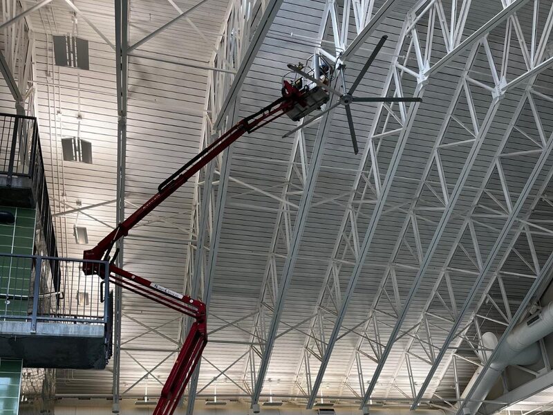 Spider lift reaching a ceiling fan above an indoor pool