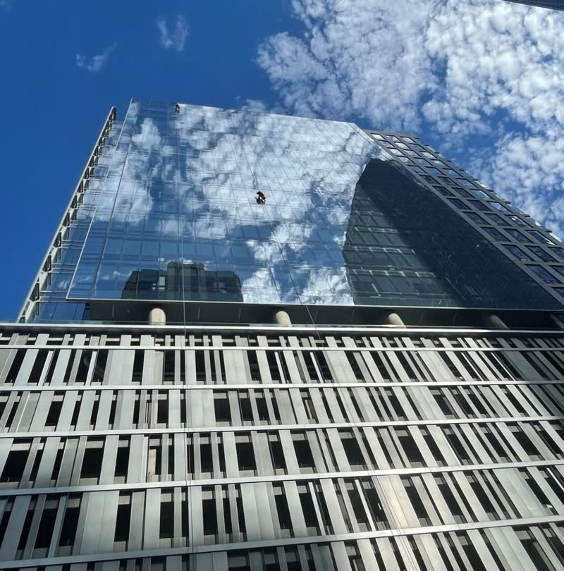 S&K rope technician on a glass curtain wall in Denver with the sky reflected in the glass