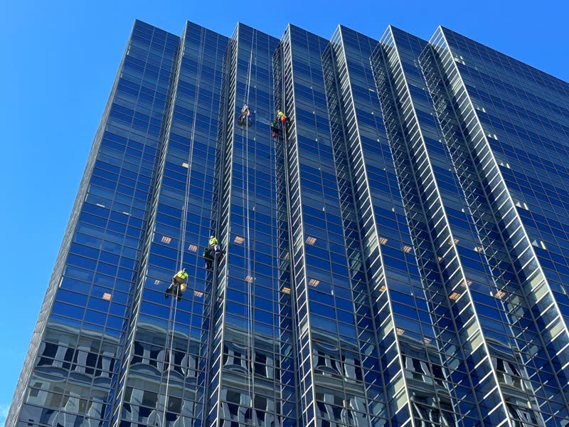 Four S&K rope technicians in hi-vis descending a blue glass tower in Denver