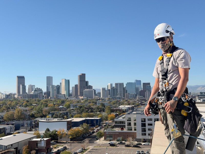 S&K rope technician in full PPE at a roof edge above Denver