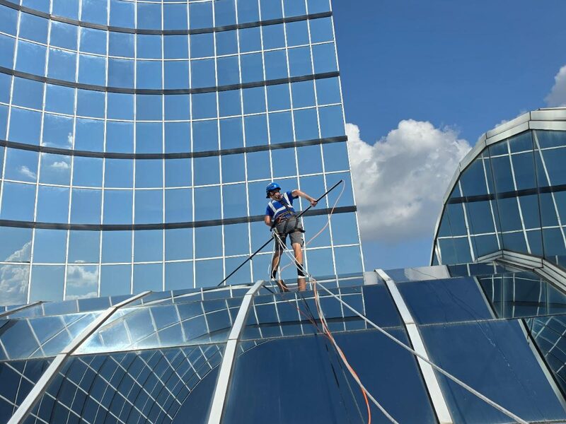 S&K technician on a curved glass canopy below a glass tower in New Orleans